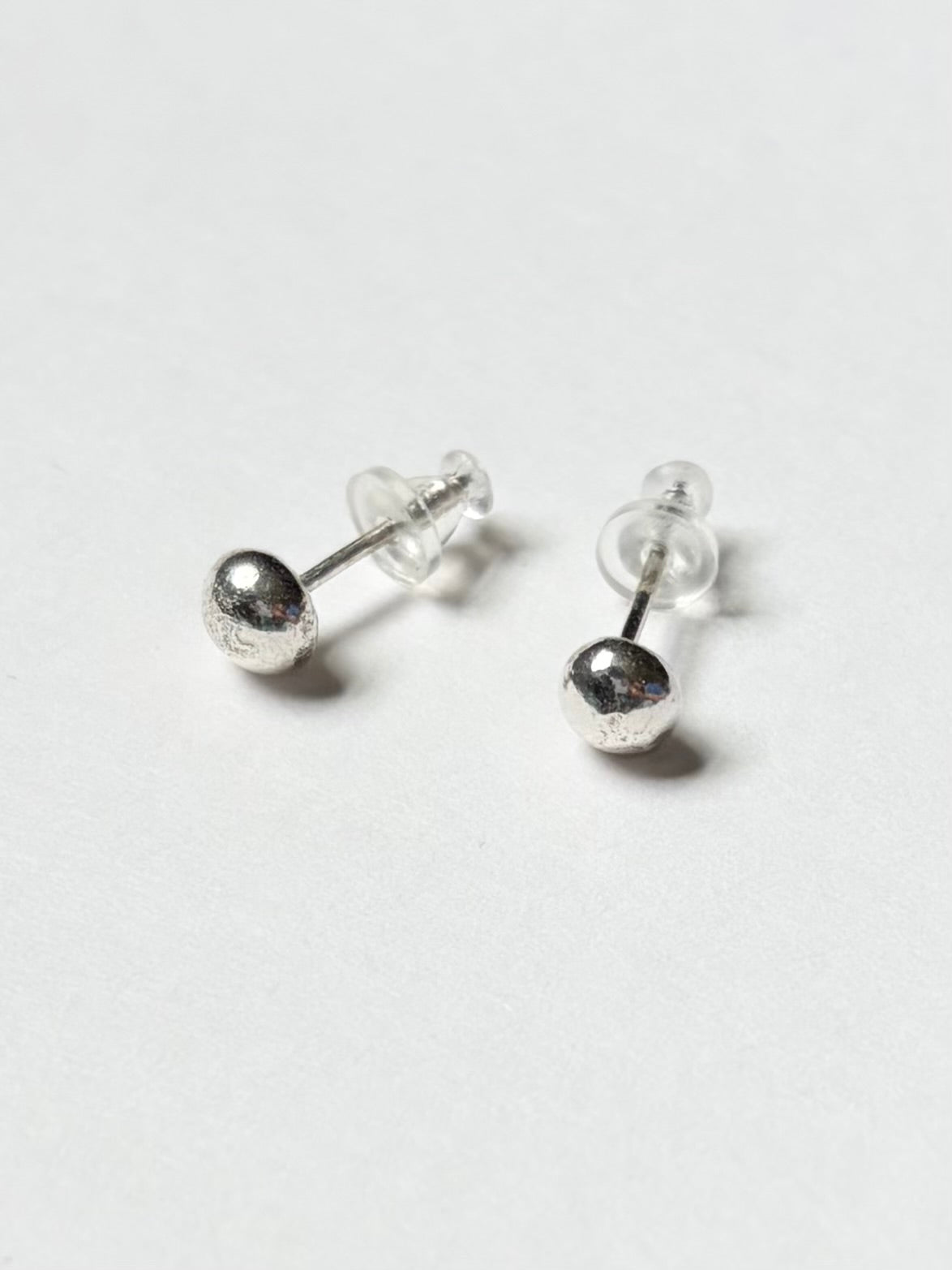 A pair of silver ball stud earrings with silicone backing, shown on a plain clean white background.