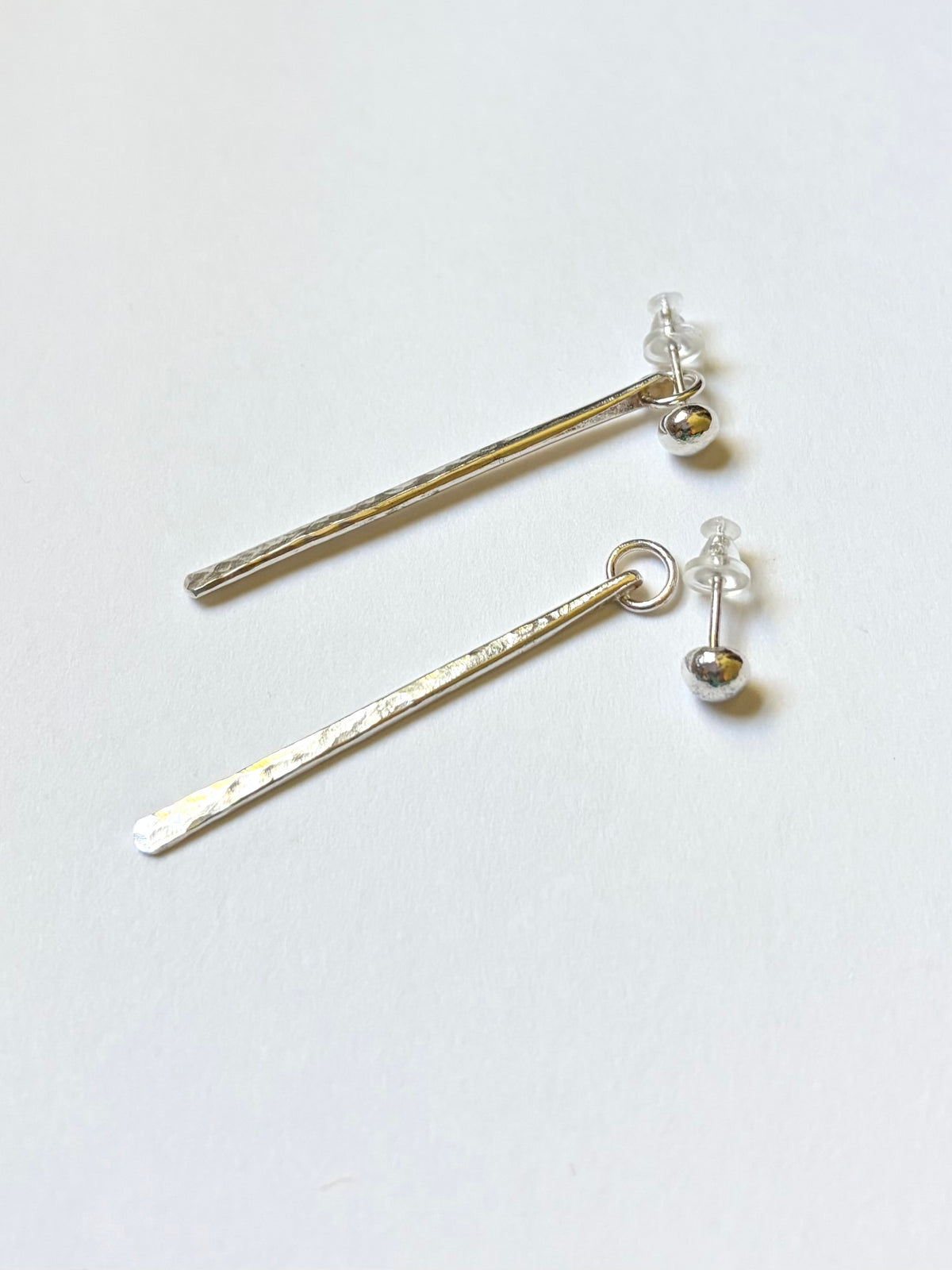A pair of silver dangle earrings with textured, hammered bar ends and small ball studs, displayed on a clean white background.