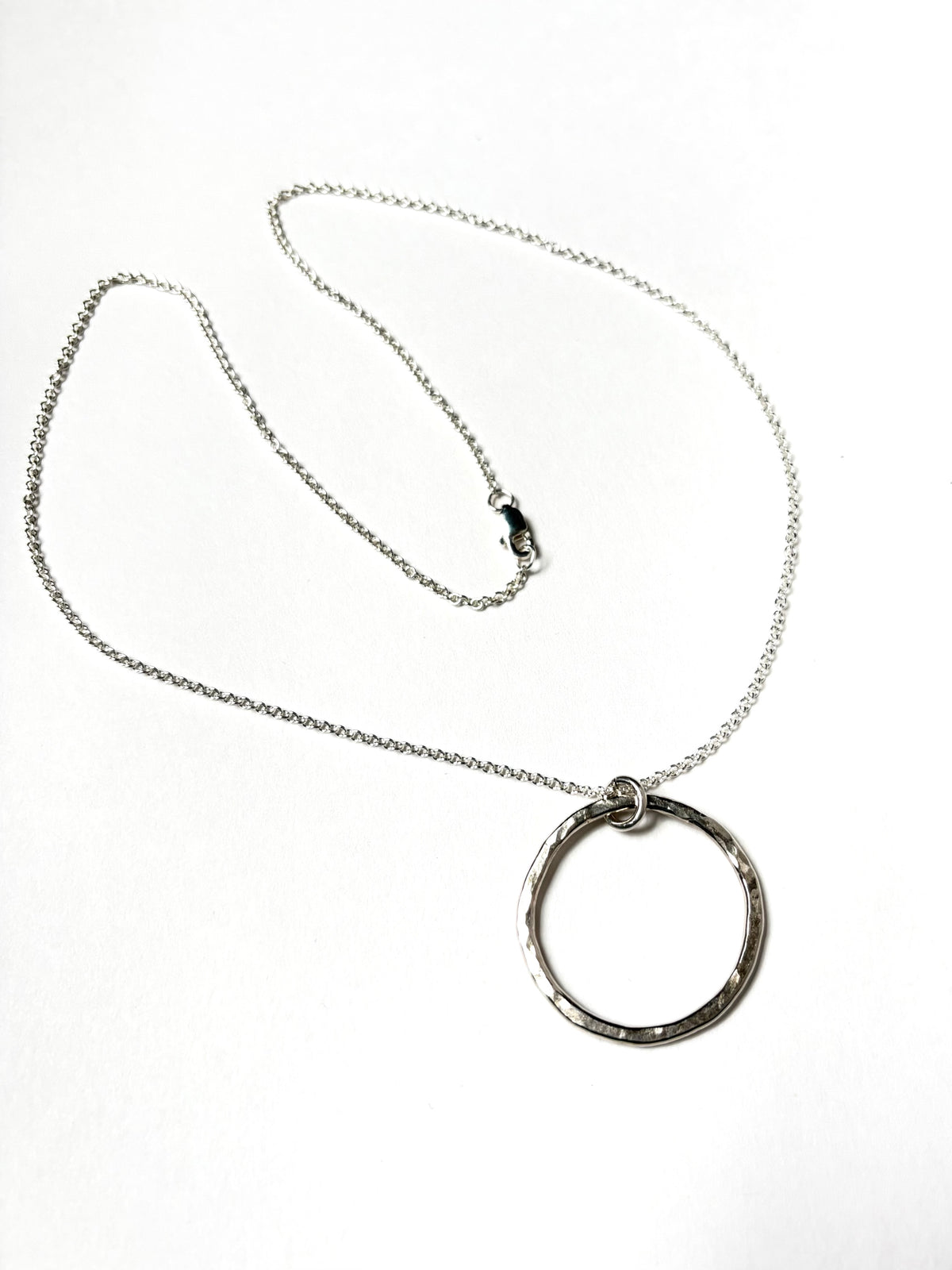 A silver chain necklace with a textured, hammered circular pendant, displayed on a clean white background.