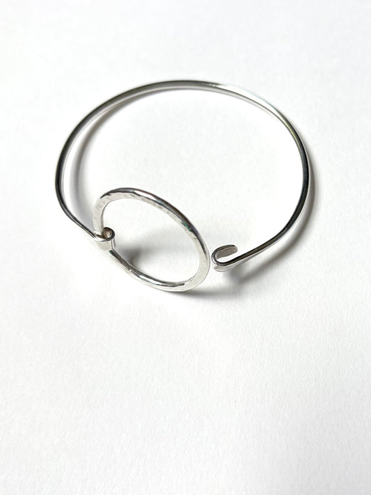 A minimalist silver wire ring bangle with a small circular loop detail, displayed on a clean white background.
