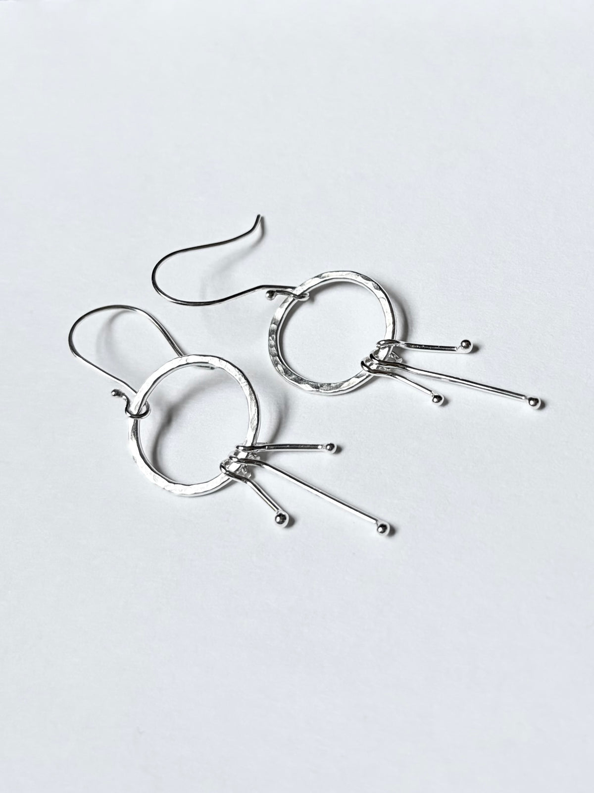A pair of silver dangle earrings with open circular hoops and three thin wire prongs ending in small beads, shown on a plain light background.
