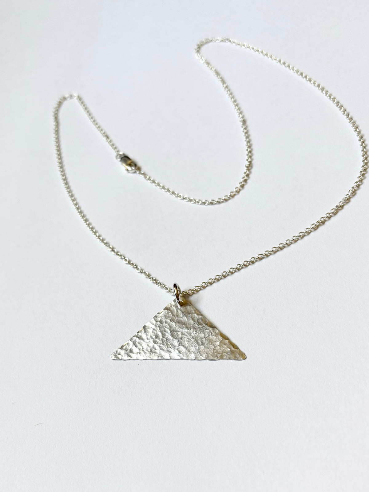 A silver chain necklace featuring a hammered triangular pendant, displayed on a clean white background.