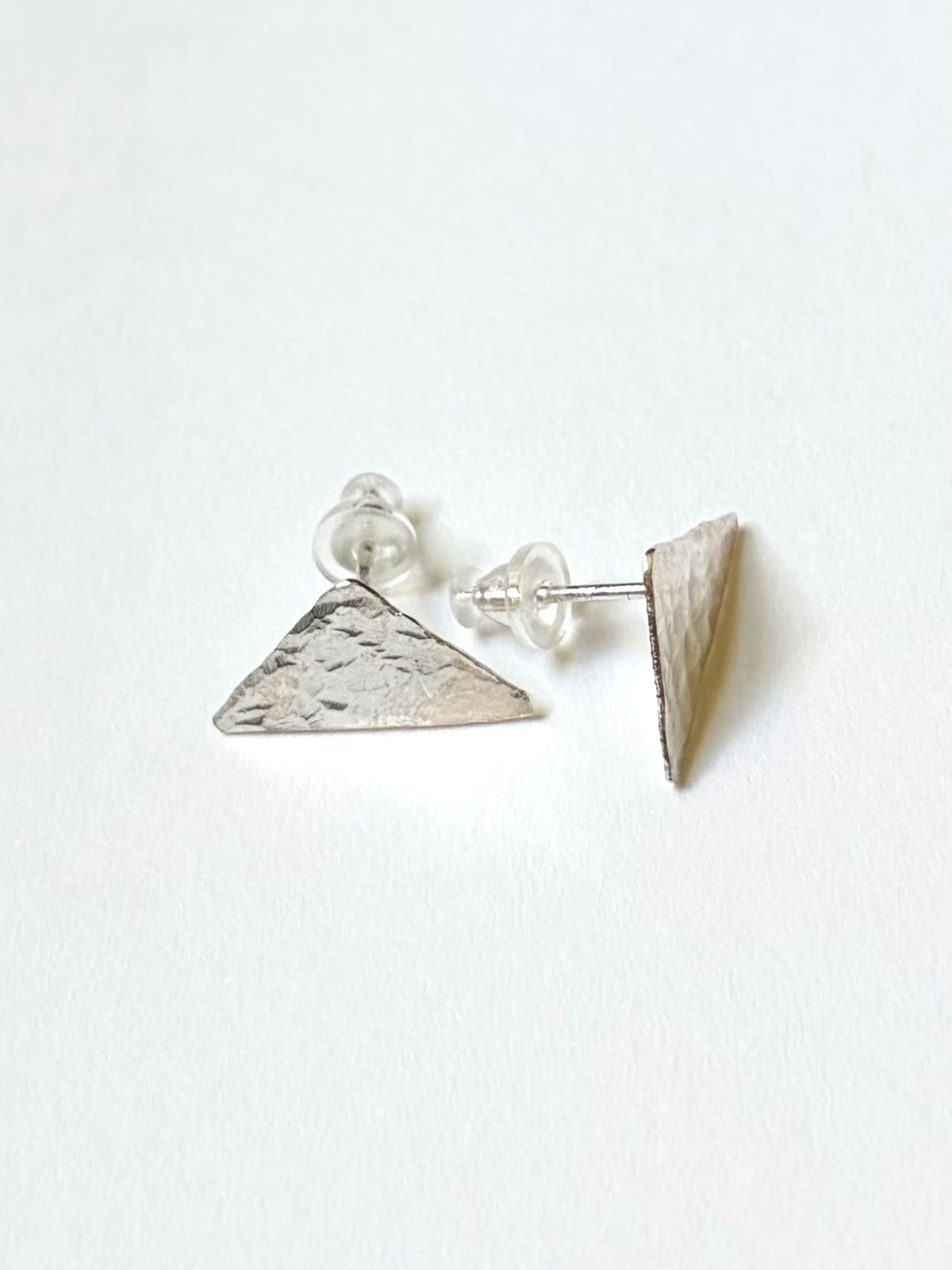 A pair of small geometric triangle stud earrings with a textured silver finish, shown on a plain white background.
