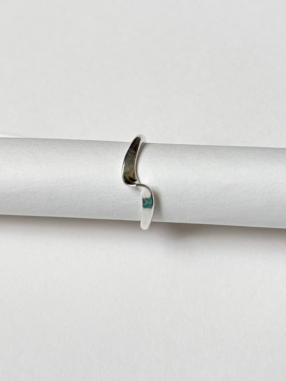 A slim silver ring, displayed on a white cylindrical ring stand against a light background.
