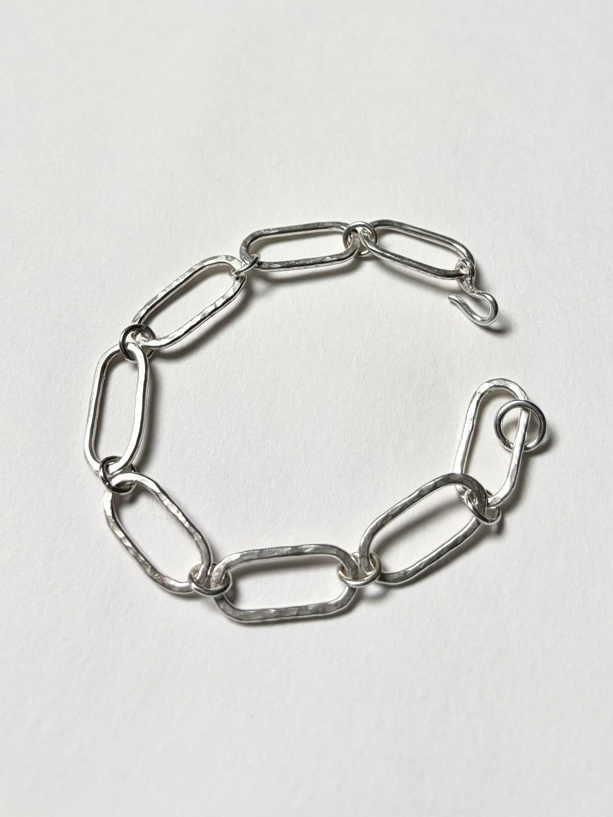 A silver paperclip chain bracelet with a textured finish and a hook closure, displayed on a clean, light white background.