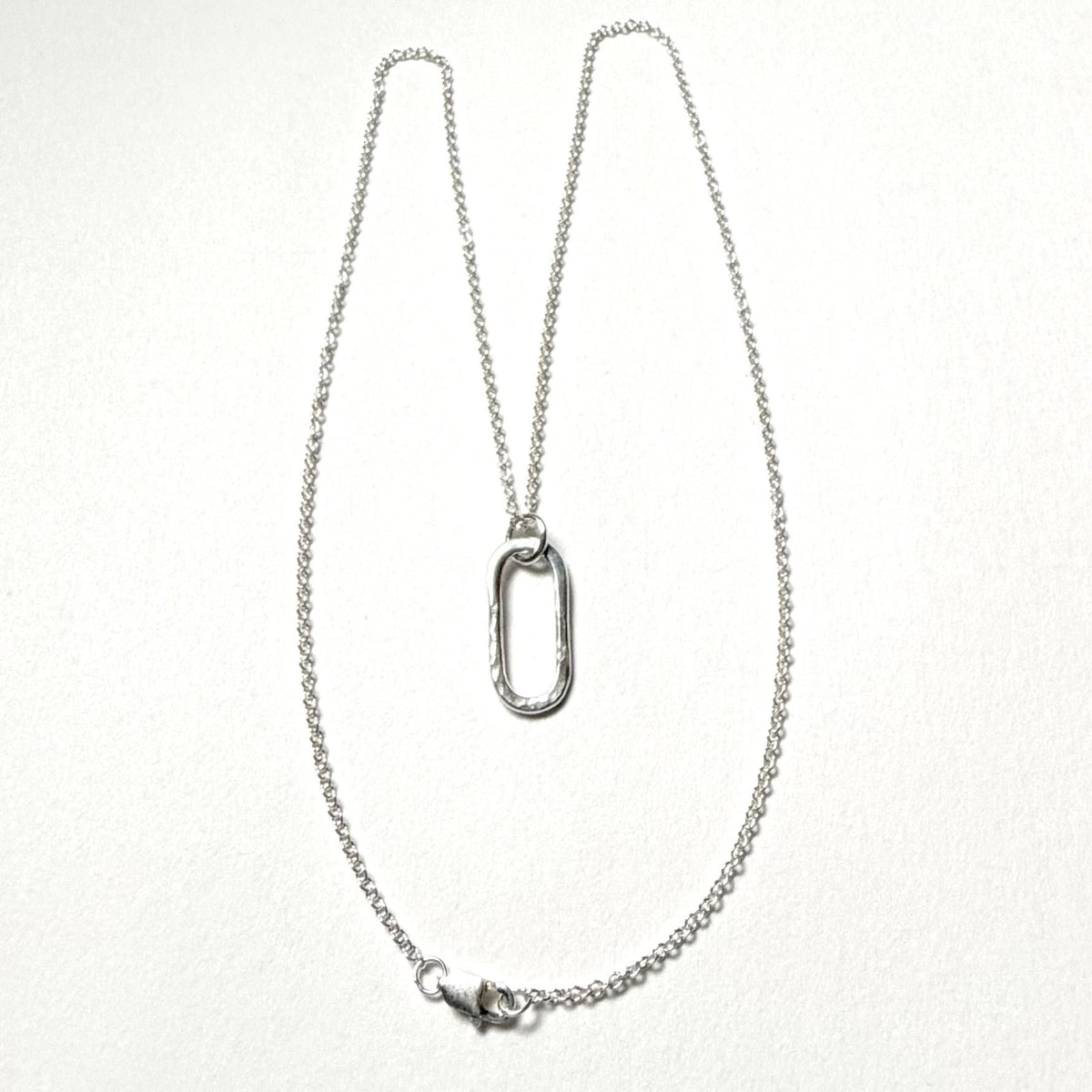 A silver chain necklace with a textured, open oval pendant, displayed against a clean white background.