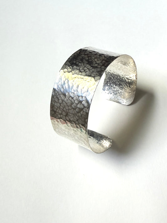 A hammered silver cuff bracelet with a textured, pebbled finish, photographed on a clean white background with a soft shadow.