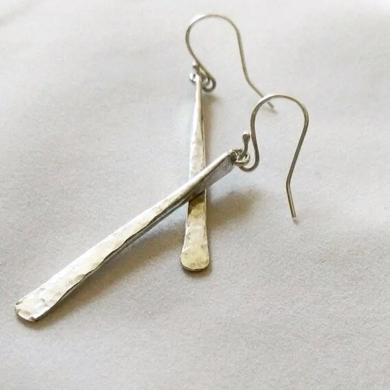 A pair of long silver bar earrings that are hammered in a way that tapers, they are shaped thinner at the top and wider at the bottom.  There is a small hoop soldered to the top of the earrings so they dangle from the silver ear wires.