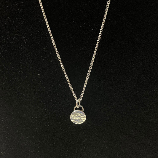 May include: Silver necklace with a hammered, circular pendant. The chain is delicate and the pendant is textured, adding a rustic touch. This minimalist necklace is perfect for everyday wear or a special occasion. The simple design makes it a versatile piece that can be styled in many ways.
