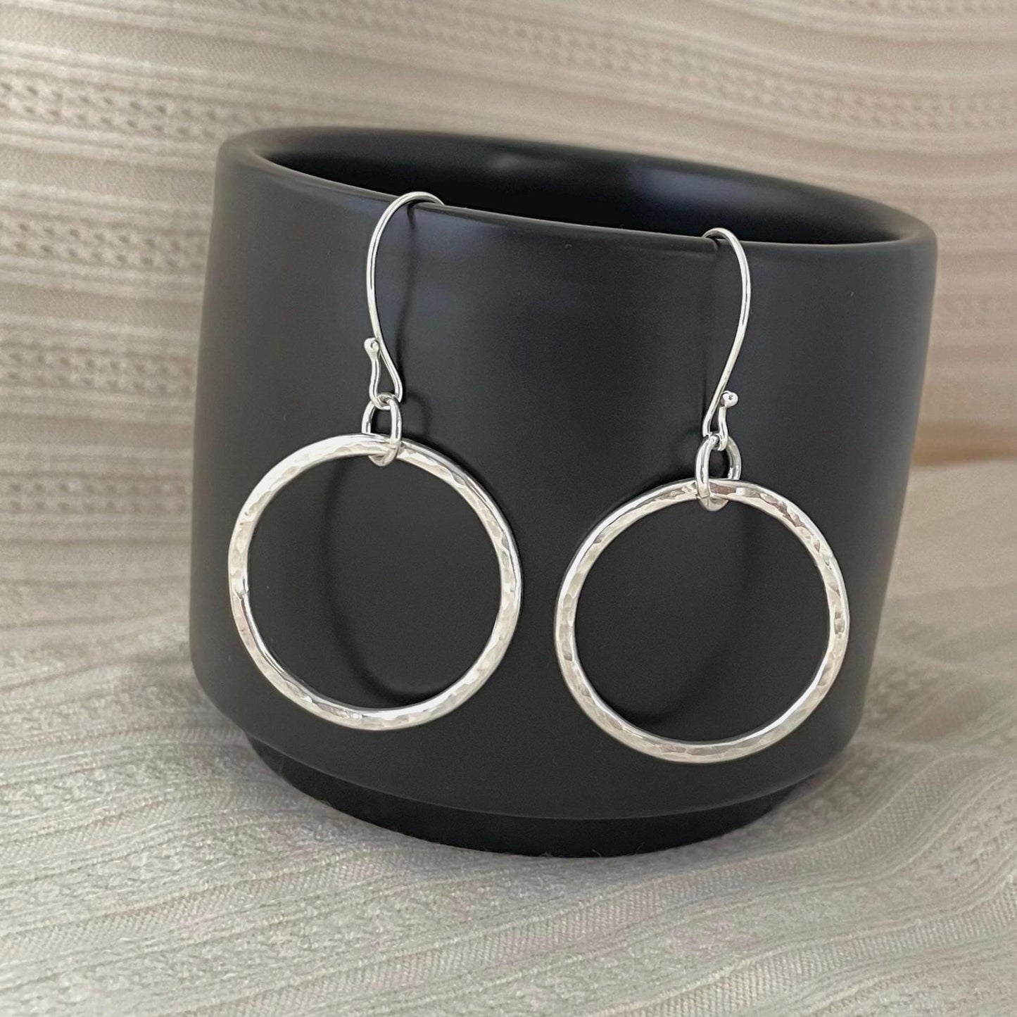May include: Silver hammered circle dangle earrings.  These lightweight earrings feature a textured, hammered finish and a simple, minimalist design. The hoops are approximately 1 inch in diameter and hang from delicate silver ear wires.  These stylish earrings are perfect for everyday wear or a special occasion.