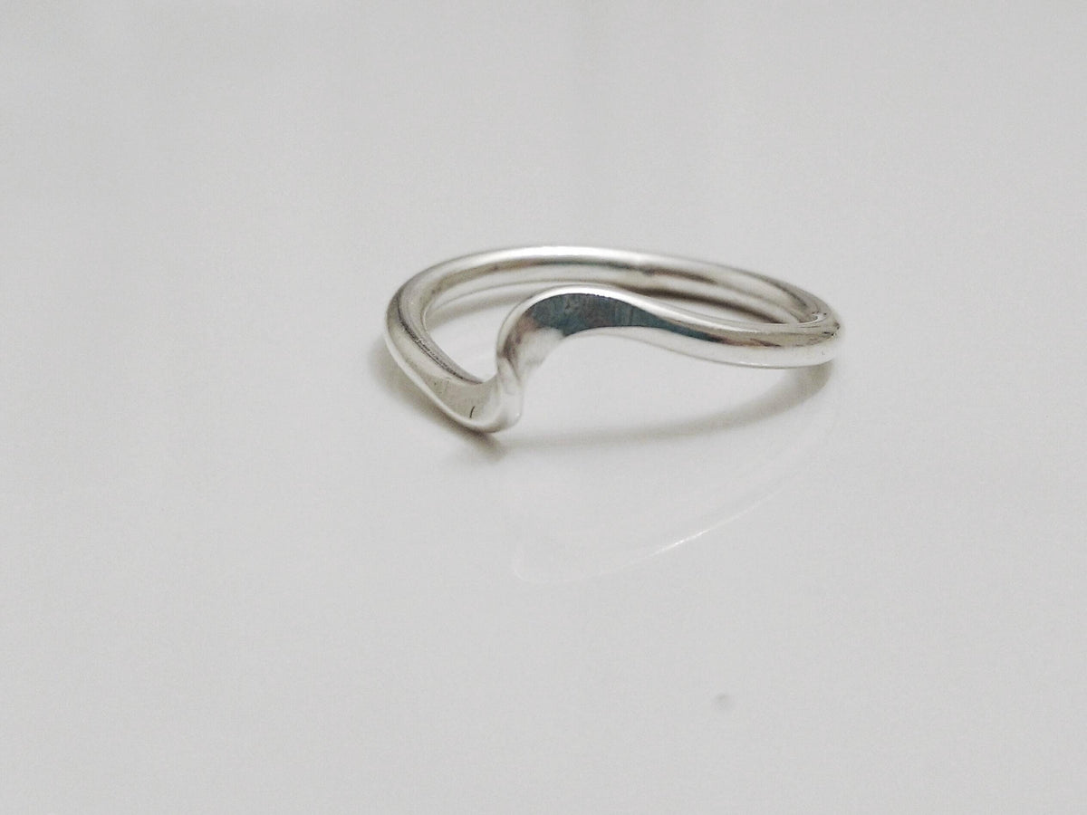 May include: A polished silver ring featuring a smooth, continuous band with a single, gentle wave-like curve along the top edge. The metal has a reflective, metallic finish, and the design maintains a consistent thickness throughout the entire circular shape.