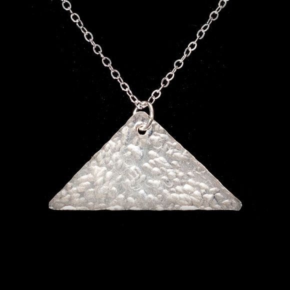 A flat, hammered, shiny, silver triangle pendant with the top corner drilled with a hole,  dangles a silver jump ring and a  silver cable chain.  The triangle is one point at top and two points at the bottom, measuring approximately one inch wide.